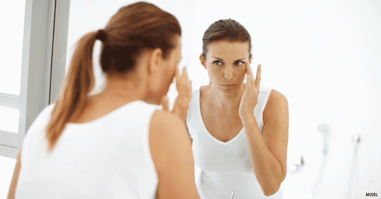 Woman with ponytail looking in mirror and applying cream