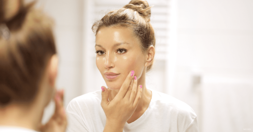 Woman with smooth and glowing skin looking in the mirror (model)