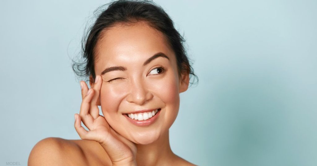 Woman blinking while gently touching the skin around her eyes. (MODEL).