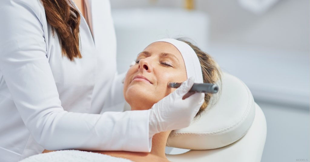 Woman receiving a facial treatment from an esthetician in a spa setting (MODELS).